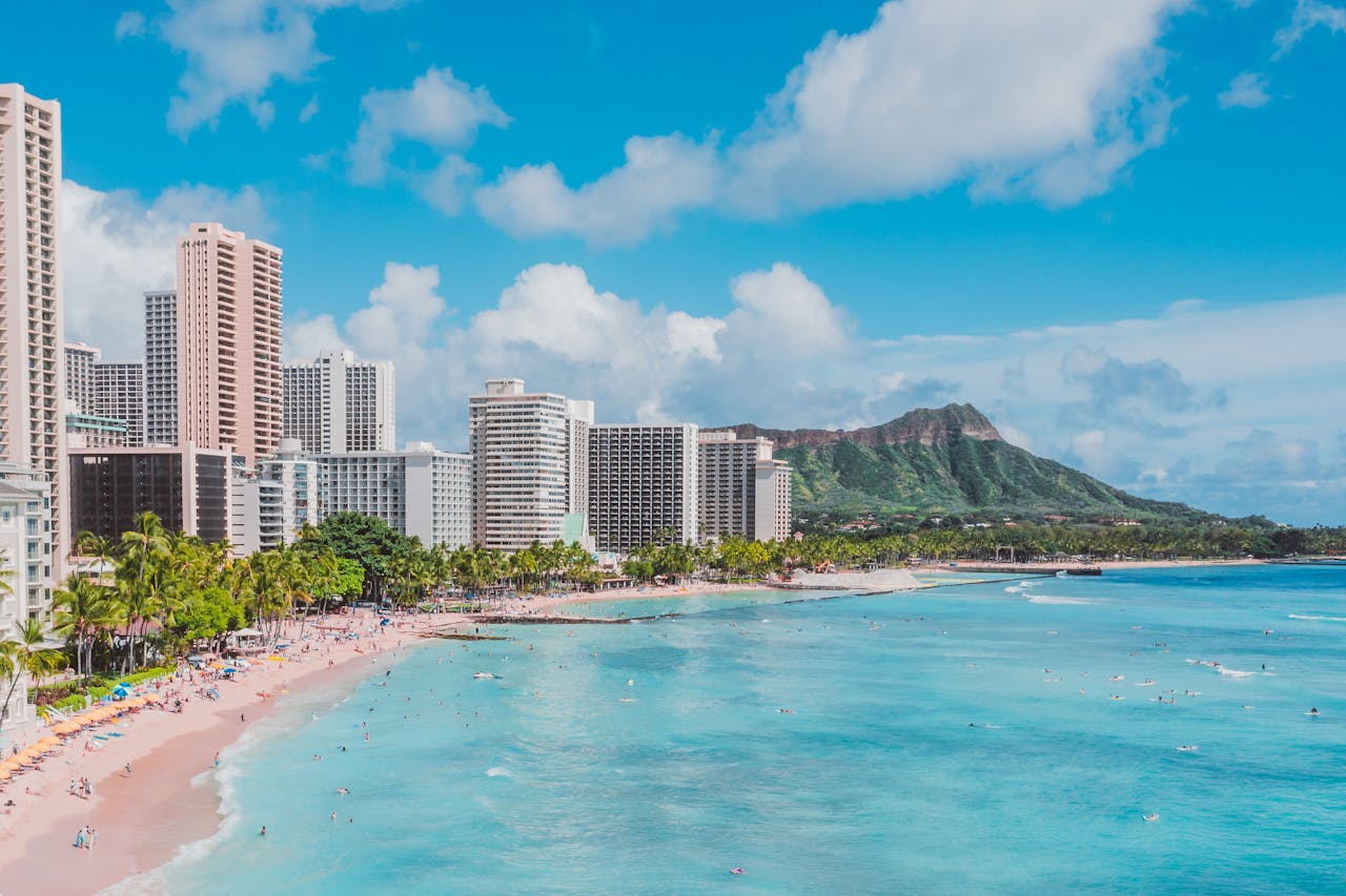 A vibrant view of Waikiki beach with people enjoying the summer and the skyline of Honolulu in the background.